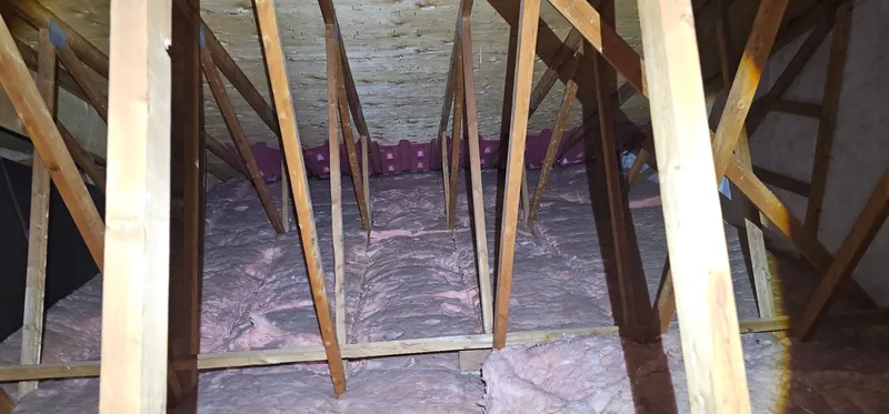 Grenier avant les travaux : nattes de laine rose tassées entre les solives, sous les fermes de toit, déflecteurs de ventilation au fond
