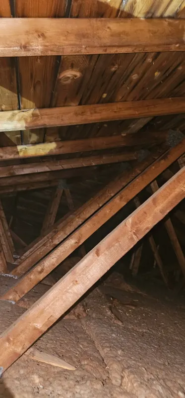 Grenier avant les travaux : ancien isolant brun, mince et tassé, sous les fermes de toit et le toit en planches