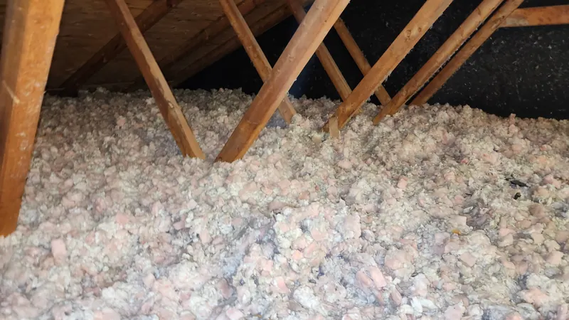 Grenier avant les travaux : ancien isolant en vrac rose et blanc, tassé et poussiéreux, entre les fermes de toit