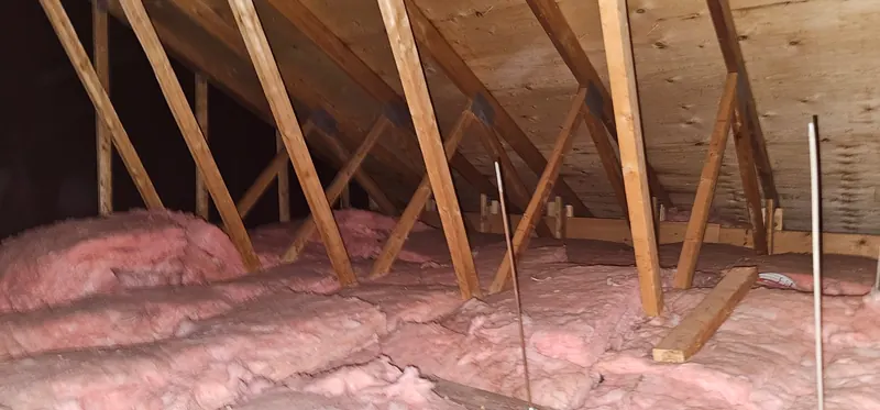 Grenier avant les travaux : nattes de laine rose, bosselées et inégales, entre les fermes de toit