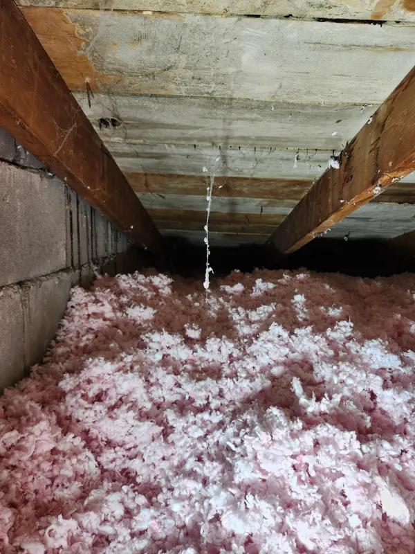 Grenier après les travaux : laine soufflée rose, épaisse et uniforme, le long du même mur de blocs de béton, sous le toit en planches