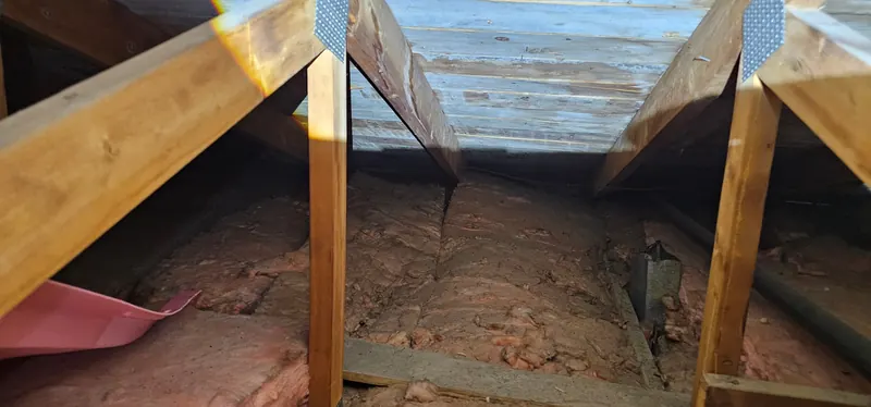 Grenier avant les travaux : vieilles nattes de laine rose, tassées et poussiéreuses, entre les fermes de toit sous un toit en planches