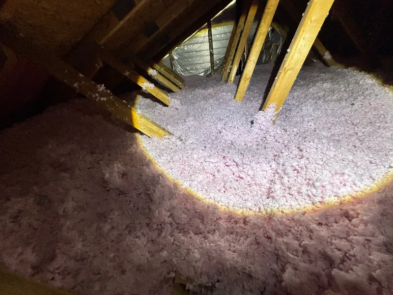Grenier après les travaux : laine soufflée rose, épaisse et uniforme, éclairée à la lampe de poche sous les fermes de toit